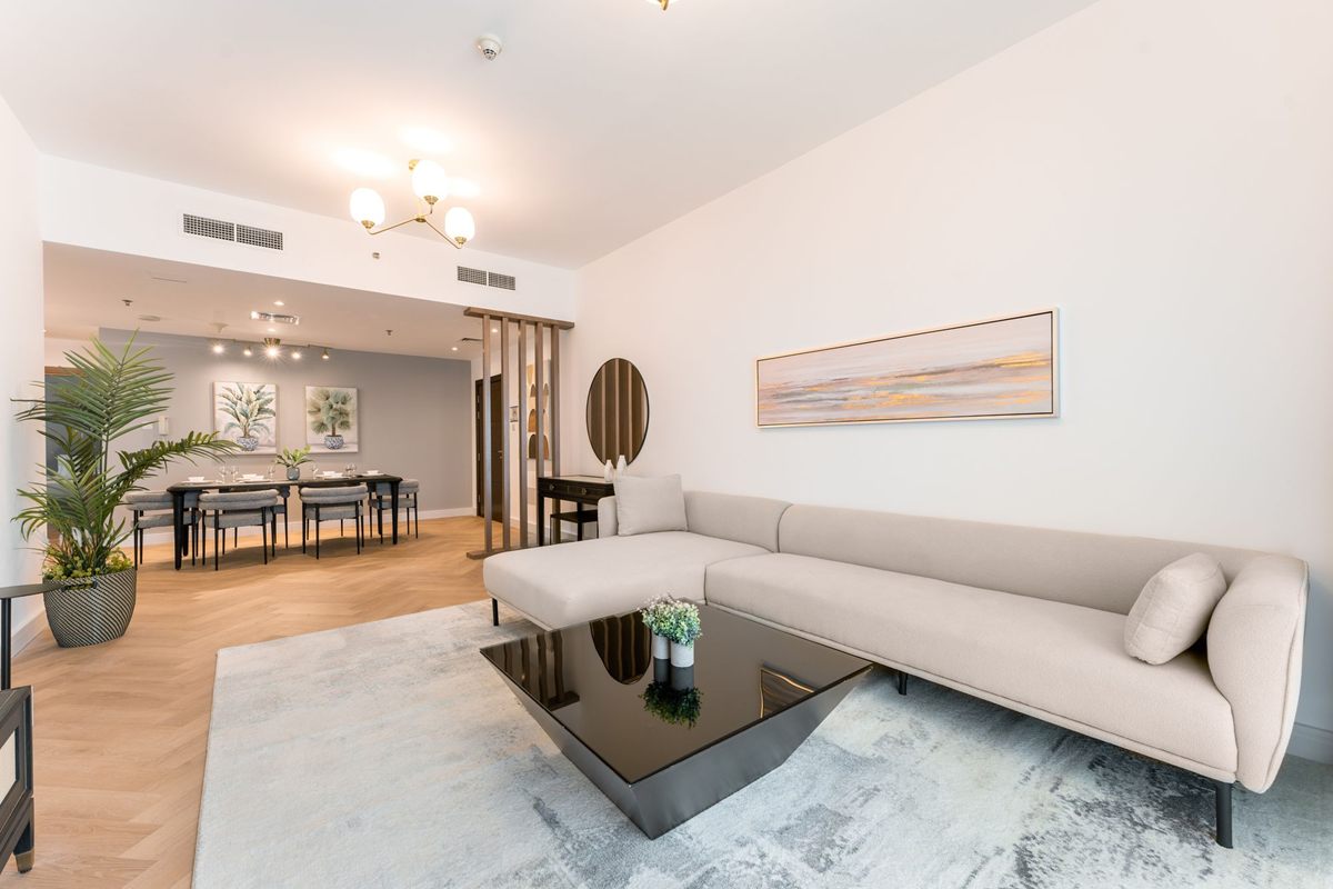 A bright living room with a pale rug, a long sofa and a dining area beyond