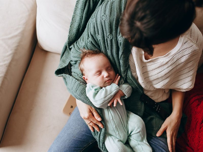 A parent holding a sleeping baby on a sofa