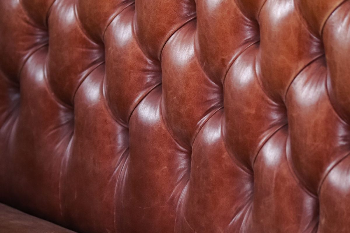 The button-tufted back of a tan leather sofa